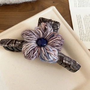 Detailed close-up of a knit flower hair claw clip with dark blue beads and plaid fabric trim