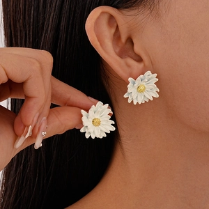 Close-up of white daisy floral stud earrings with gold stamen on model's ear