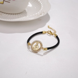 Macro detail of gold-plated Virgin Mary charm with cubic zirconia on black cord bracelet