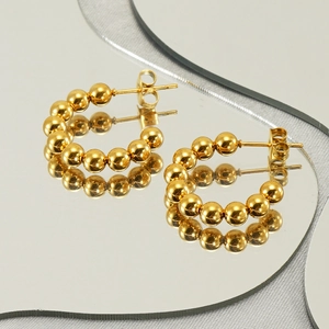 Elegant gold beaded C-shape hoop earrings reflected on a mirror with silk background