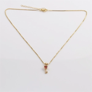Close-up of gold heart-shaped key pendant with red crystal and lobster clasp chain