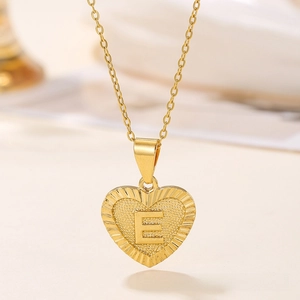 Macro view of gold heart pendant with engraved rays and letter E on cross chain