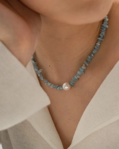 Close-up of titanium steel necklace with light blue stones and a white pearl on a model