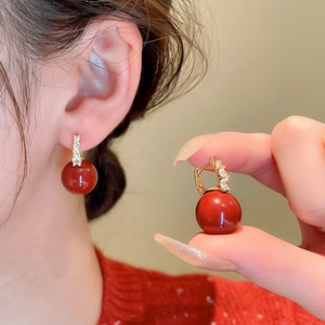 Détail de boucles d'oreilles créoles dorées avec perles rouges et zircons scintillants