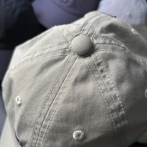 Détail de la calotte d'une casquette beige avec œillets brodés et bouton supérieur