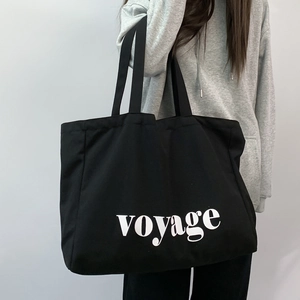 Close-up of black canvas tote bag with white voyage lettering carried by a model