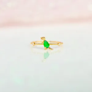 Macro view of 18K gold dinosaur ring featuring a green pear-cut stone and beaded band