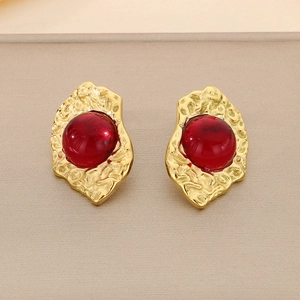 Macro shot of gold-plated vintage earrings with red cat-eye stone and hammered texture