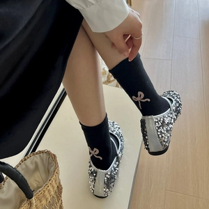 Close-up of black mid-calf socks with pink bows paired with silver sequin Mary Jane shoes