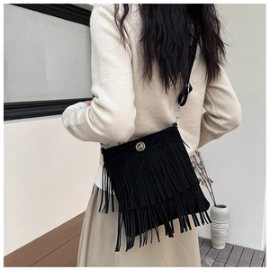 Detail of a chic black suede crossbody bag with elegant fringe and metallic round buckle