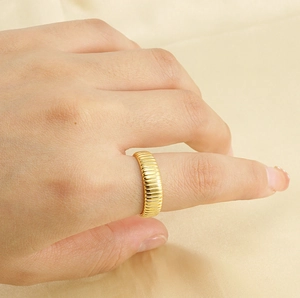 Close-up of a gold textured ring on a finger with warm satin background lighting