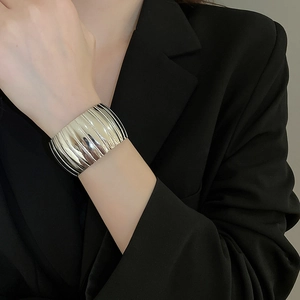 Macro view of wide silver metallic cuff bracelet featuring vertical pleated texture details