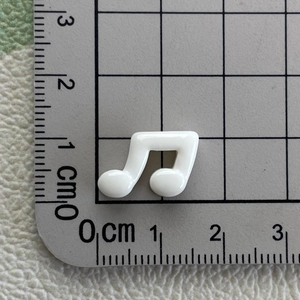 Close-up of a white glossy musical note resin charm measured on a cutting mat scale