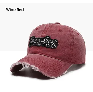 Detail of burgundy baseball cap featuring Purist embroidery and distressed ripped brim edge