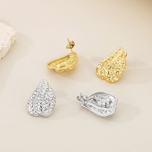 Detailed view of textured gold and silver irregular heart earrings on a beige surface