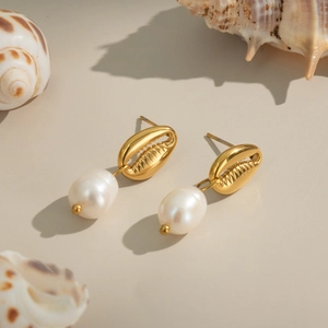 Détail de boucles d'oreilles dorées en forme de coquillage avec perles blanches pendantes