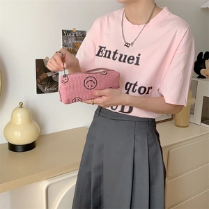 Close-up of pink corduroy pouch with embroidered smileys held in a lifestyle setting