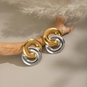 Minimalist interlocked gold and silver stainless steel hoop earrings on a wood branch