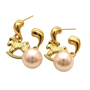 Élégantes boucles d'oreilles cheval à bascule doré avec grandes perles blanches sur fond blanc