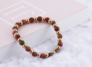 Detail of gold titanium beads and red stone beads on a pink textured background