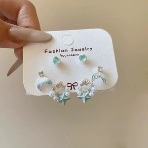 Close-up of ocean-themed earrings featuring mermaid tail, seashell, and pearls on a card