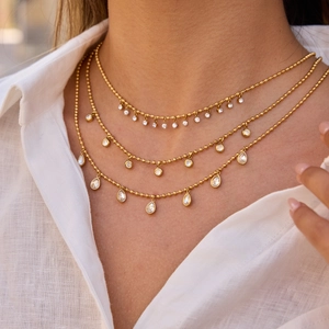 Three-layer gold beaded necklace with clear zircon pendants on elegant white linen shirt