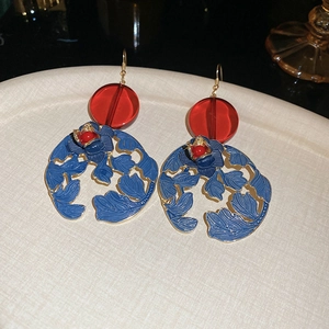 Close-up of blue flower enamel earrings with red beads on a beige textured plate