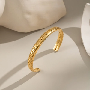 Dettaglio macro della trama intrecciata dorata su un bracciale rigido in acciaio