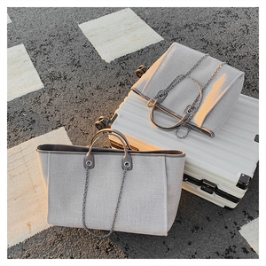 Close-up of gray woven tote bag with metal chain strap on pavement by suitcase
