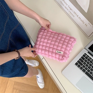 Pink bubble textured makeup bag with Sozakka brand label being held on a white desk
