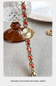 Vue détaillée de la montre bracelet dorée avec maillons en cristal rouge et cadran rond