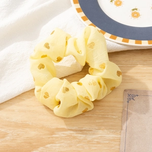 Close-up of yellow fabric scrunchie with gold heart patterns on a wooden desk