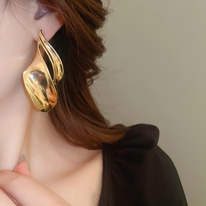 Close-up of model wearing abstract large golden wavy earrings with high-gloss finish