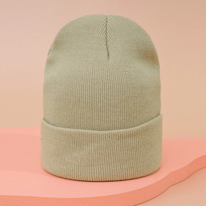 Close-up of sage green knitted beanie with fine stitch texture on a pink wave display