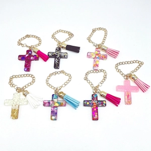 Macro detail of seven colorful resin cross charms with gold chains and leather tassels