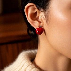 Detailed view of red apple stud earrings with gold plating and cubic zirconia on a model