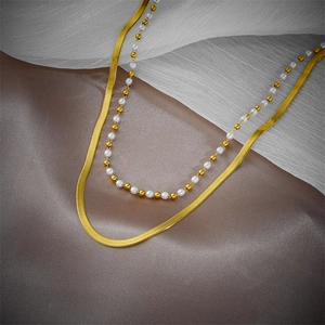 Double-layered golden snake chain necklace with white beads on silky draped fabric