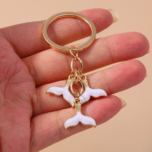 Porte-clés doré avec d'élégants pendentifs en queue de baleine émaillés blanc et or