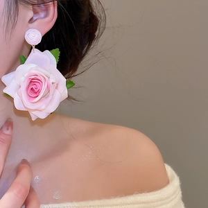 Close-up of pink fabric rose earring with green leaves on model for a romantic spring look