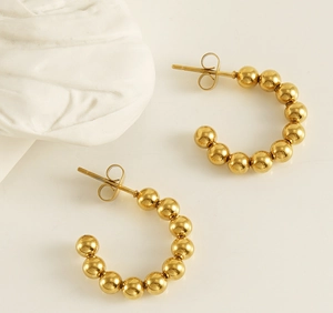 Macro detail of French vintage 18K gold bead C-shaped earrings on a white surface