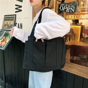 Minimalist black canvas tote bag with multiple pockets shown in a cozy cafe setting