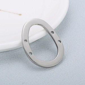 Silver stainless steel oval geometric jewelry connector with four holes on a textured surface