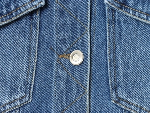 Macro shot of blue cotton denim fabric texture with yellow stitching and metal button