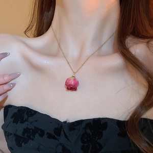 Detail of elegant gold chain necklace with pink dried rosebud pendant on model neck