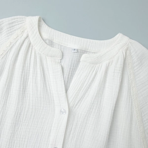Dettaglio di camicia bianca in cotone con pizzo, scollo a V e delicati bottoni trasparenti