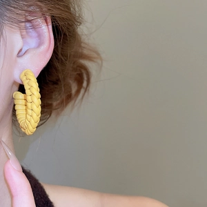 Detailed view of yellow woven C-shaped earrings worn on model for a trendy fashion look