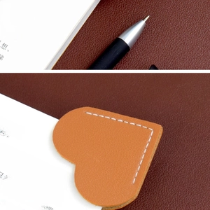 Close-up of an orange heart-shaped leather bookmark with hand-stitched details on a book page