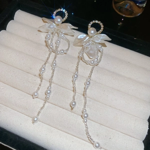 Detailed close-up of floral pearl earrings with elegant long tassels on beige velvet