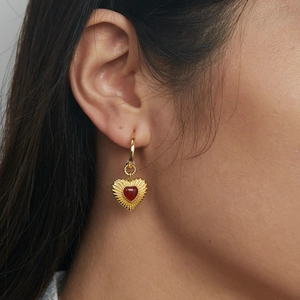 Close-up of 18k gold plated hoop earring with red heart charm pendant on female ear