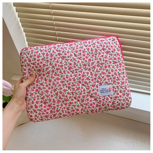 Detailed view of pink floral quilted laptop sleeve held by hand near a sunny window